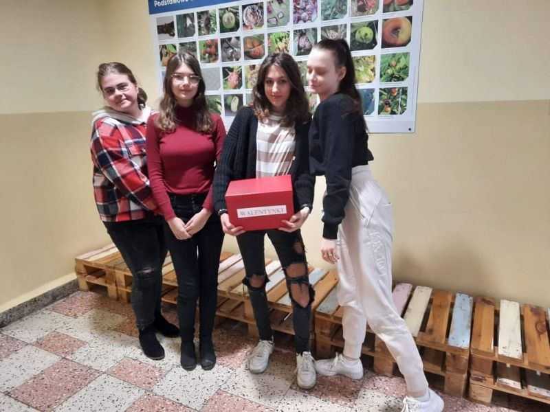 Cztery uczennice stojące na korytarzu szkolnym .Jedna z nich w ręku trzyma czerwone pudełko z napisem Walentynki