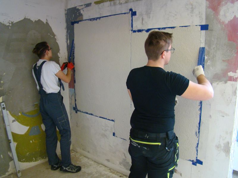 Dwóch uczniów przygotowuje ścianę do malowania