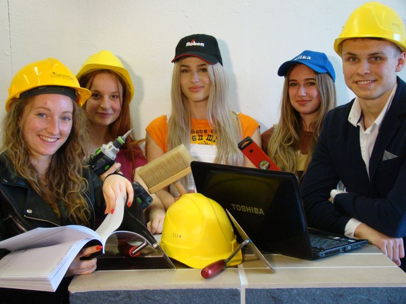 Uczniowie technikum budowlanego w żółtych kaskach z laptopem wiertarką i pędzlem malarskim