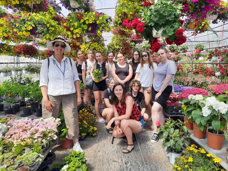 Grupa młodzieży z opiekunami w szklarni pełnej kolorowych kwiatów