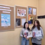 Dwie dziewczynki z dyplomami i nagrodami na tle wystawy z pracami