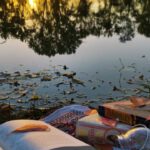Na zdjęciu na pierwszym planie leżą książki wśród liści na drugim planie drzewa o zachodzie słońca odbijające się w tafli jeziora